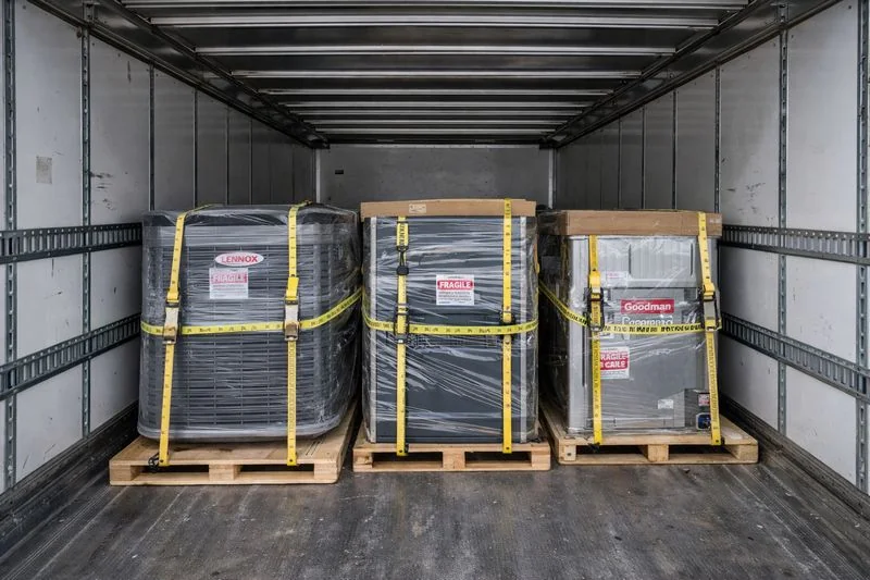 Dry van trailer with palletized HVAC equipment secured with straps for safe transport.